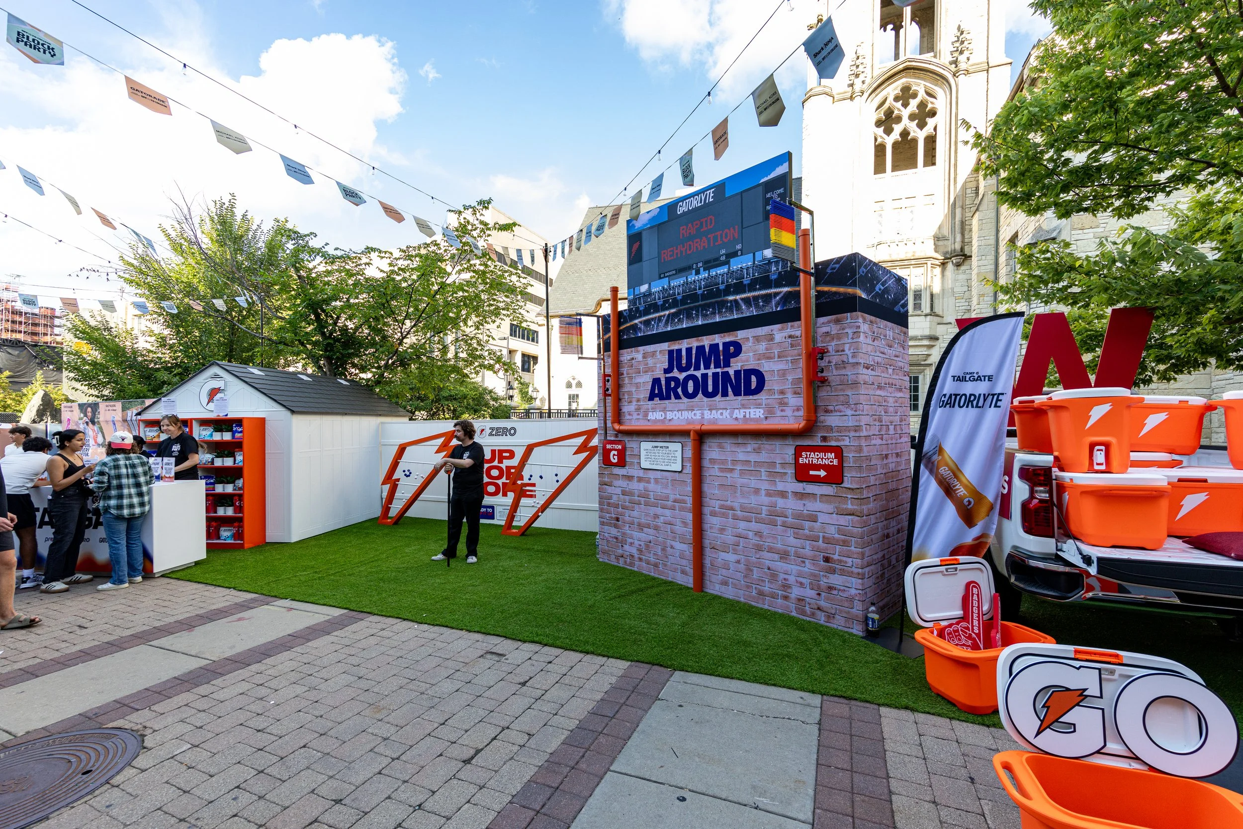 Outdoor event featuring Gatorade branding with a large digital screen displaying 'Rapid Rehydration' and 'Jump Around' signage, trees, people participating, and Gatorade equipment.