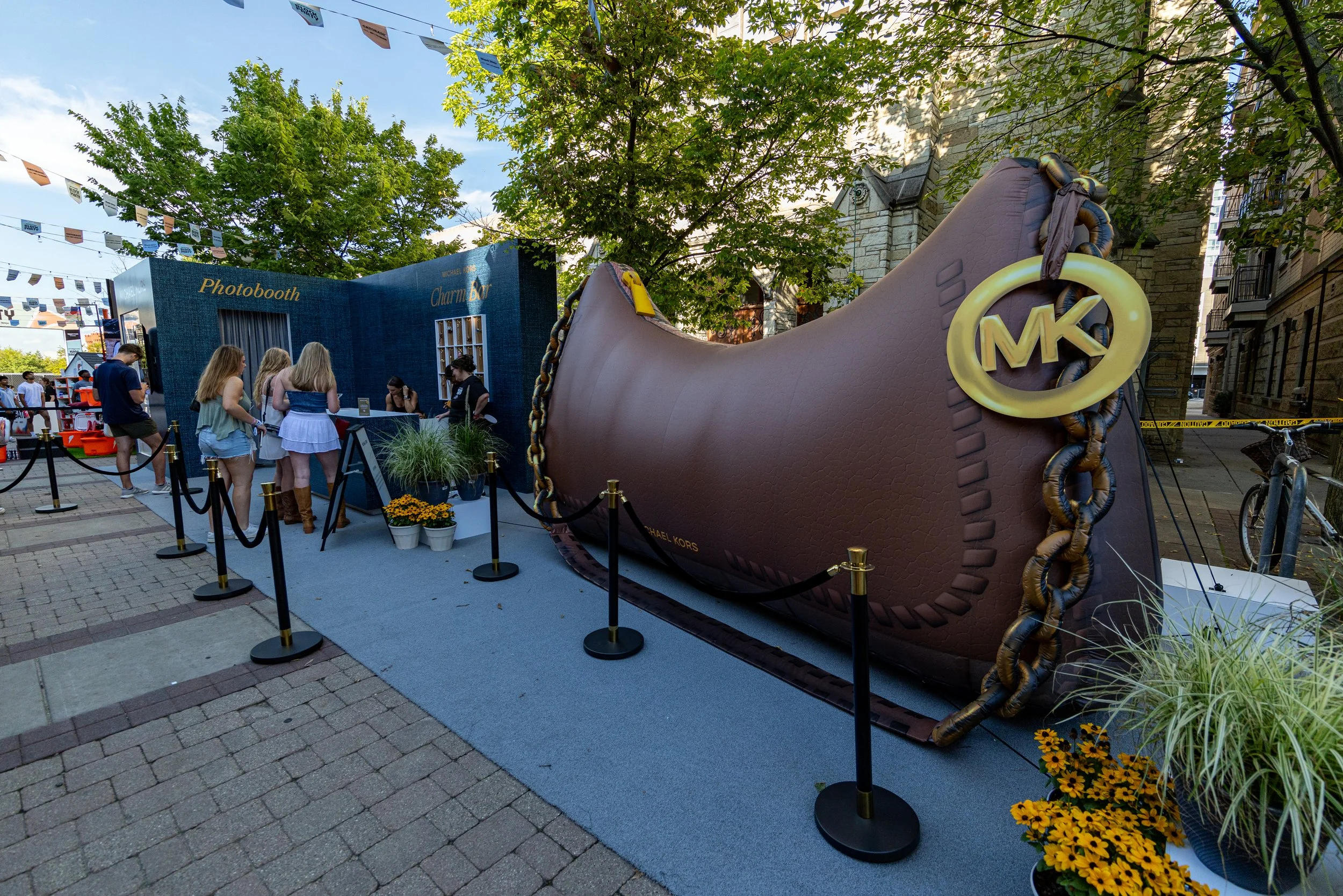 People at a photo booth with a large Michael Kors shoe prop and Charmin Bear backdrop, family and friends taking photos outdoors on city street.