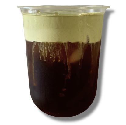 A transparent cup containing a layered drink with dark coffee at the bottom and a green creamy foam on top.