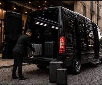 A man loading luggage into the back of a black van parked on a cobblestone street.