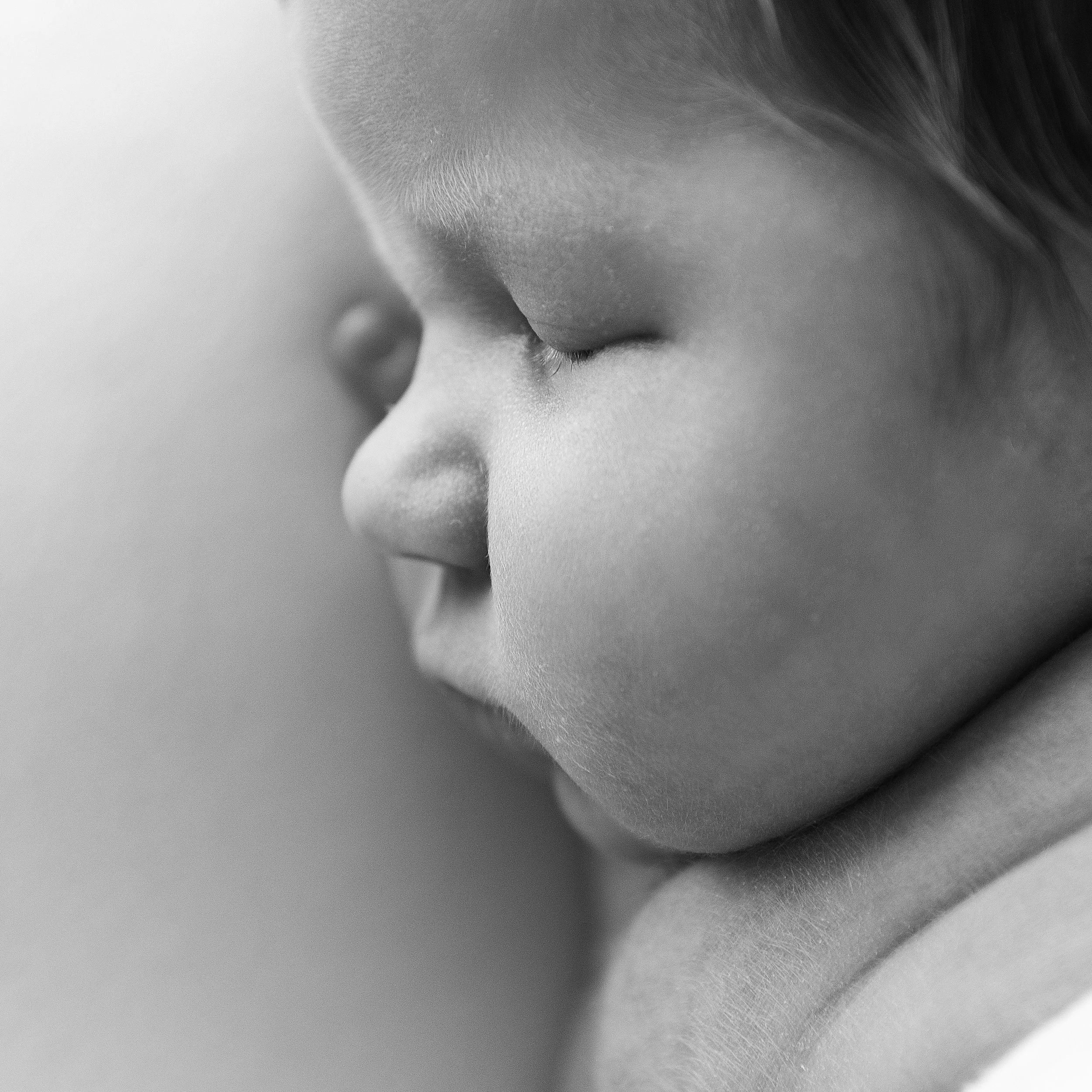 Close-up black and white image of a person's nose and part of their face, with soft focus and textured skin.