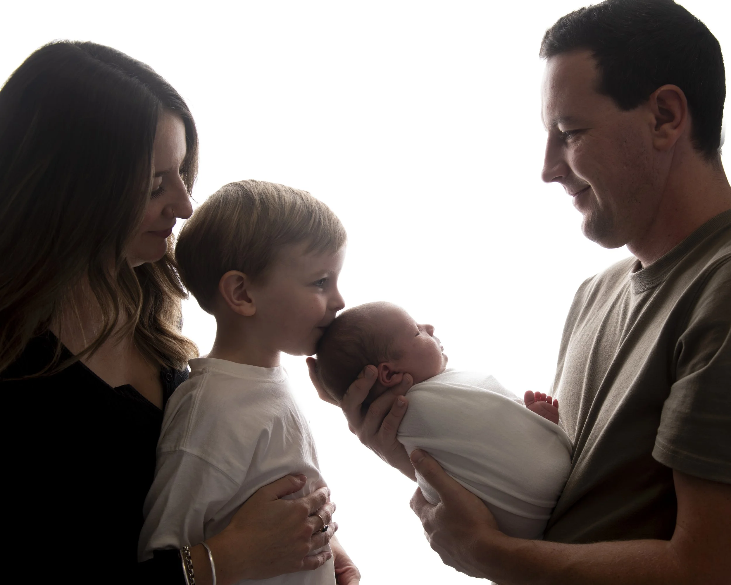 A family holding their two newborn babies, with the mother and father smiling and looking at each other, and the children looking at the parents.