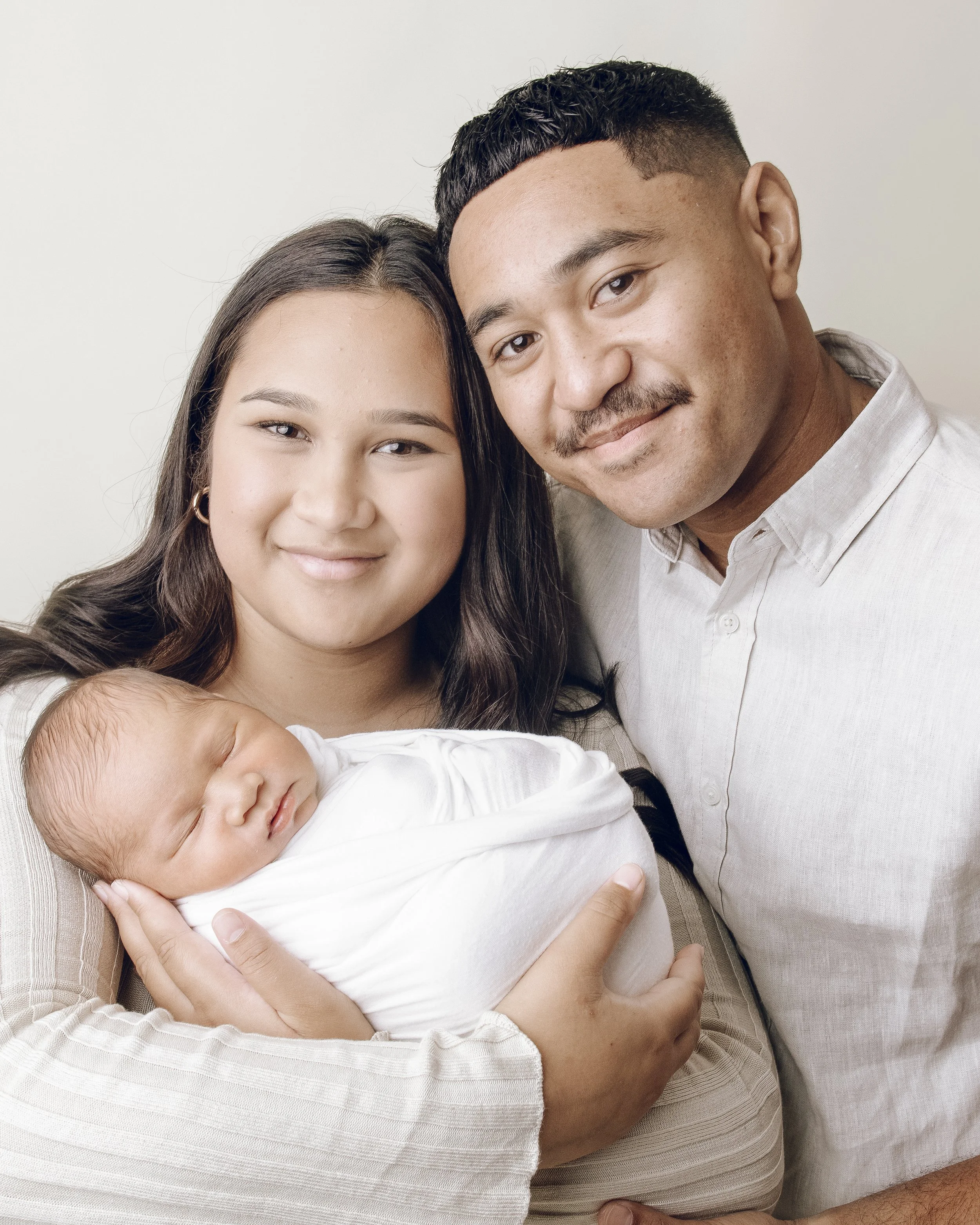 A diverse family poses for a close-up photo with a woman holding a newborn baby, and a man smiling.