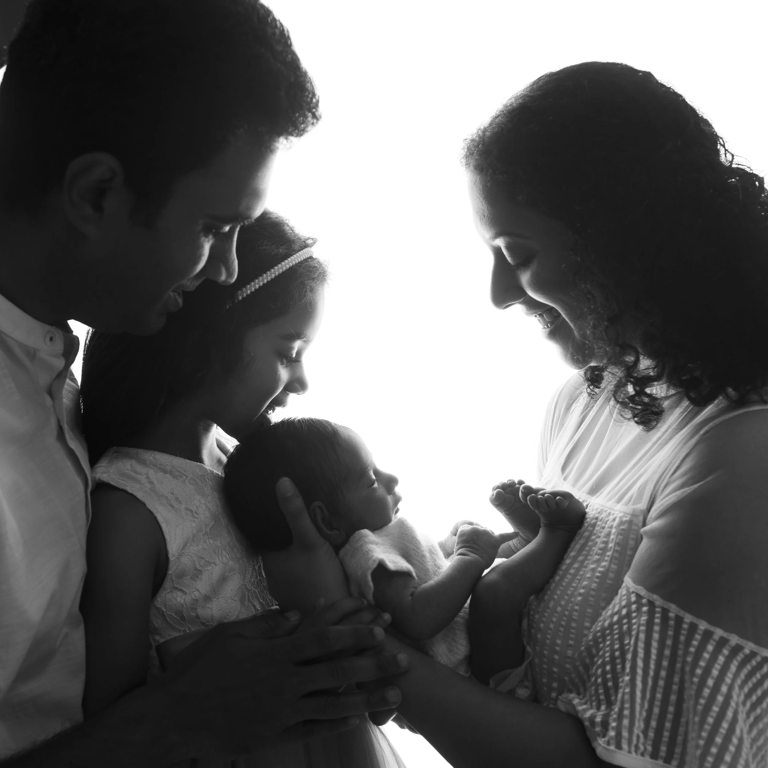 A black and white photo of a family, including a mother, father, and children, with their foreheads touching and their eyes closed, expressing love and connection.