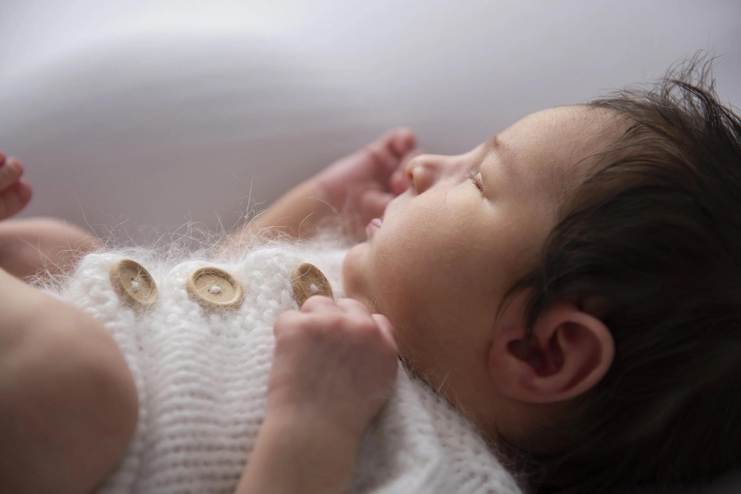 Close-up of a baby lying on a knitted blanket with wooden buttons, peacefully sleeping with closed eyes and dark hair.