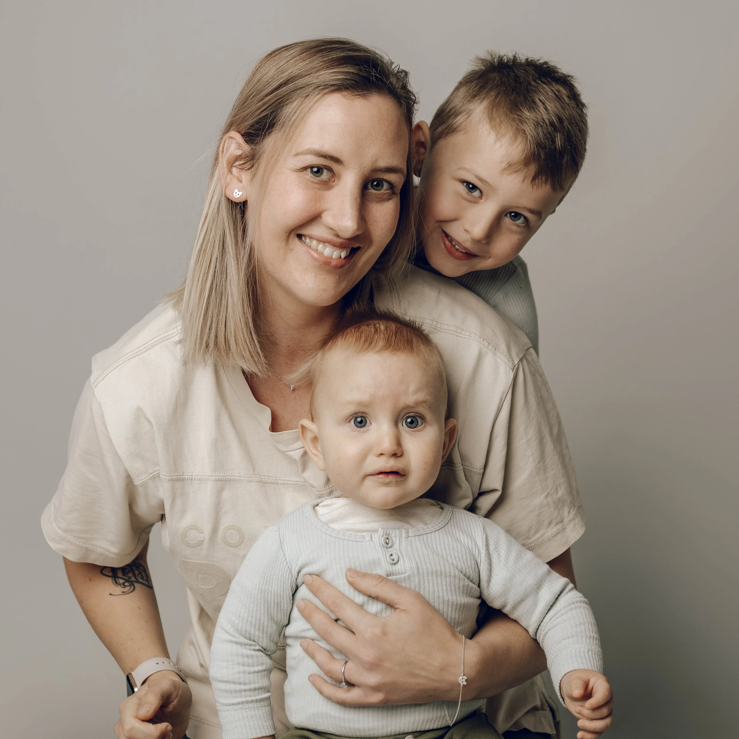 A woman smiling and hugging a young boy against a plain grey background.