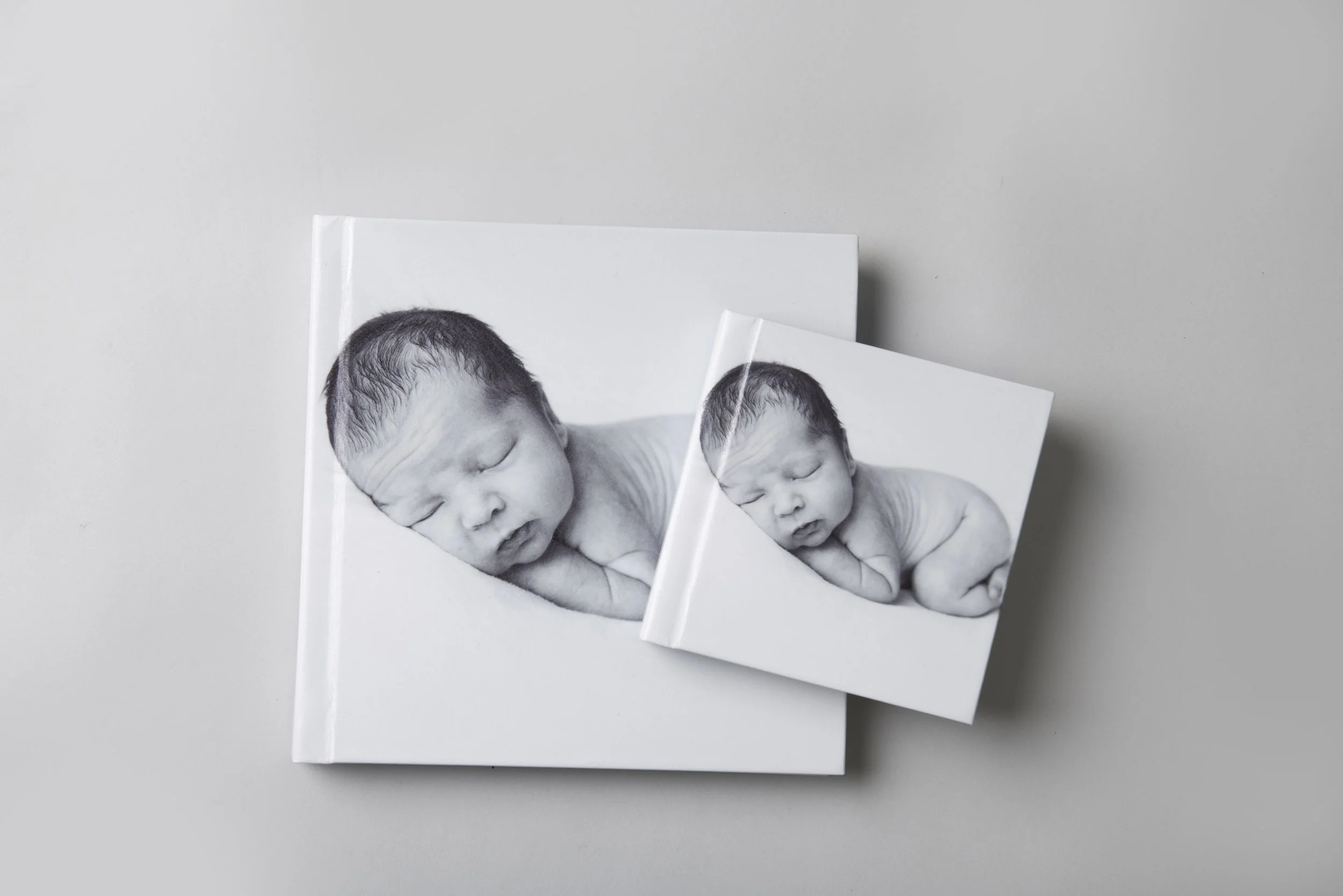Close-up image of two white books featuring black-and-white photographs of a sleeping newborn baby on both covers.