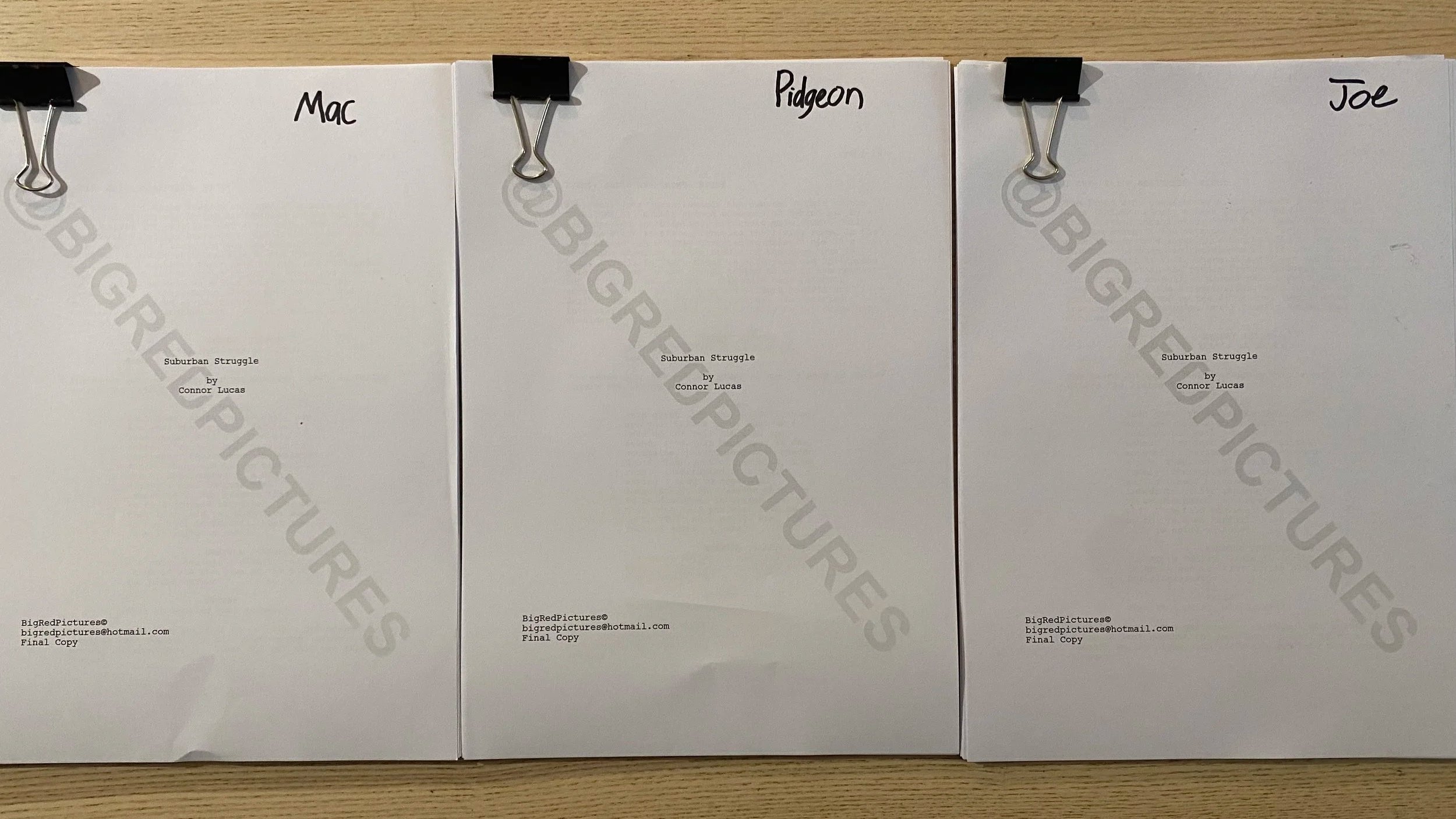 Three white printed books titled 'Suburban Struggle' by Connor Lucas, held together with black binder clips, arranged upright on a wooden surface.