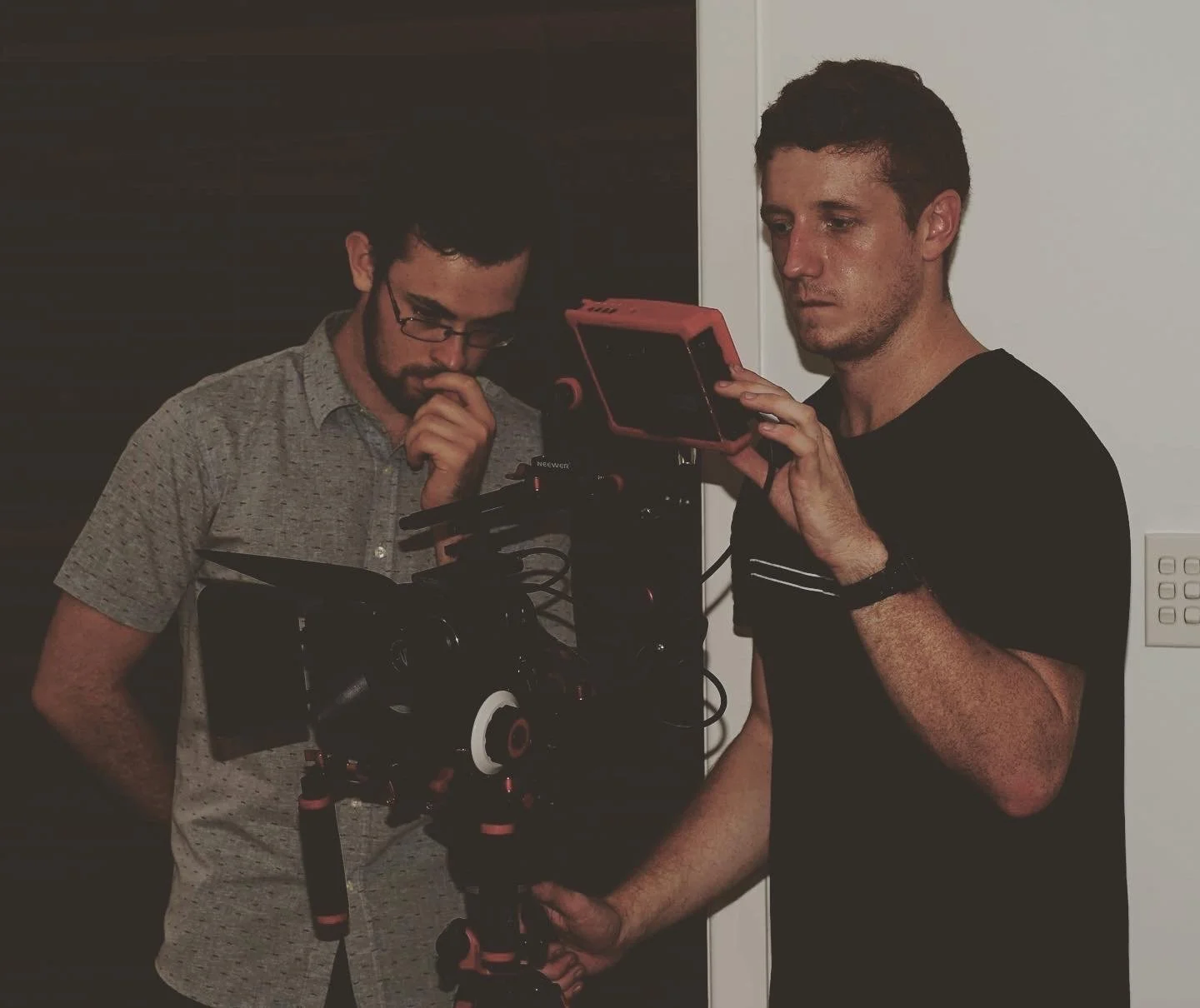 Two men working with a camera and monitor in a dimly lit room.