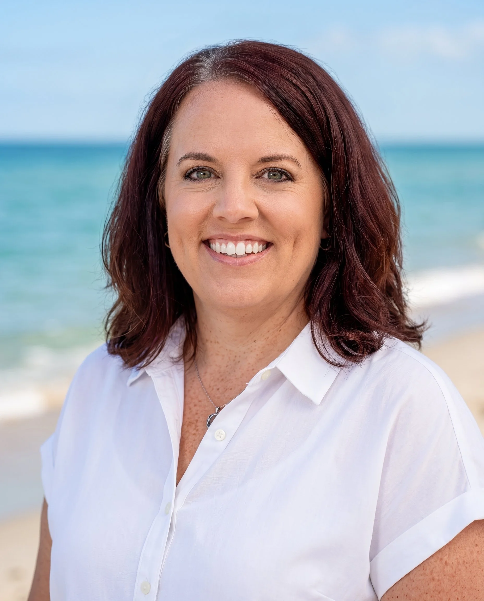 Close-up of a woman smiling at the beach, with ocean and sky in the background.