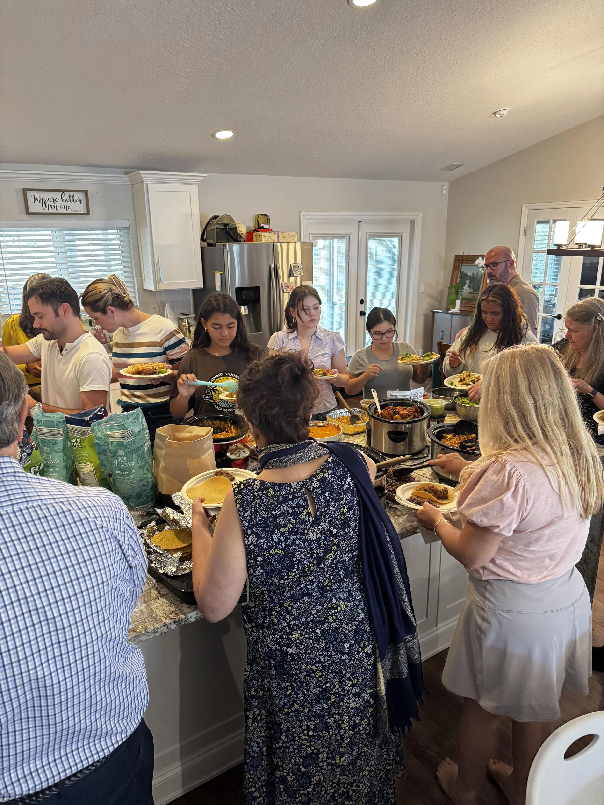 Group of people standing around a kitchen counter serving themselves food at a buffet-style meal.