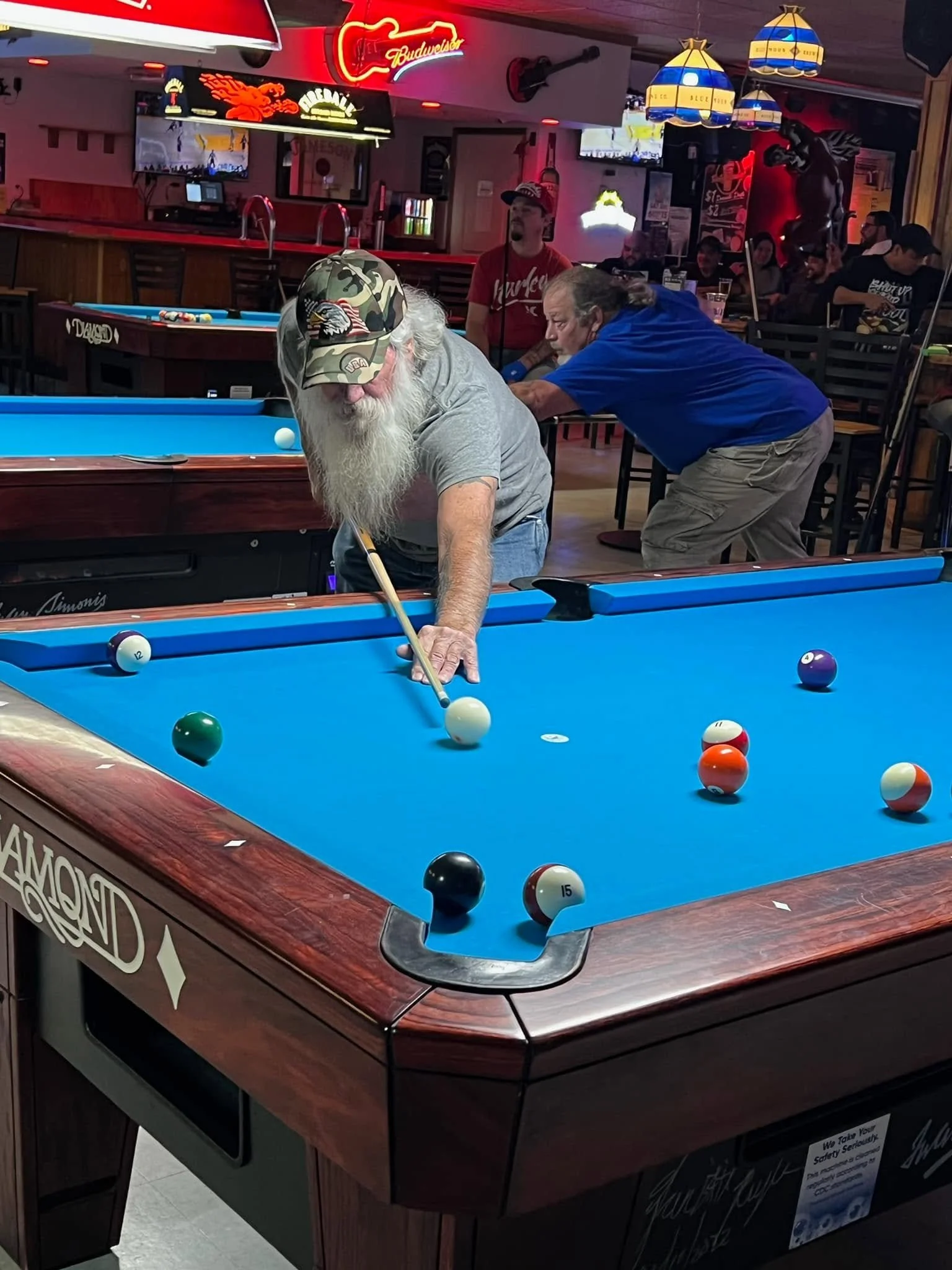 A group of people playing pool in a bar or recreational venue with neon lights and advertisements.