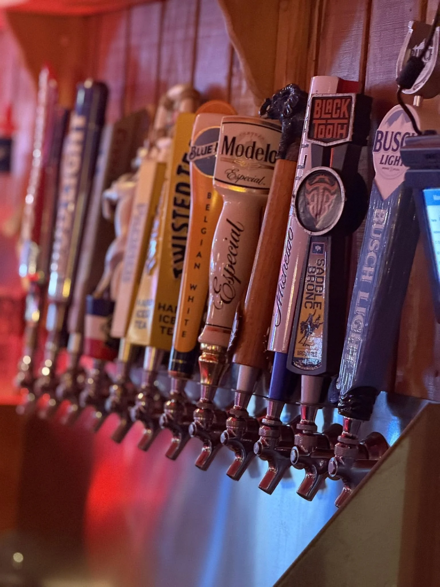 A row of beer tap handles mounted on a bar, featuring various brands including Modelo, Bud Light, and Blue Moon.