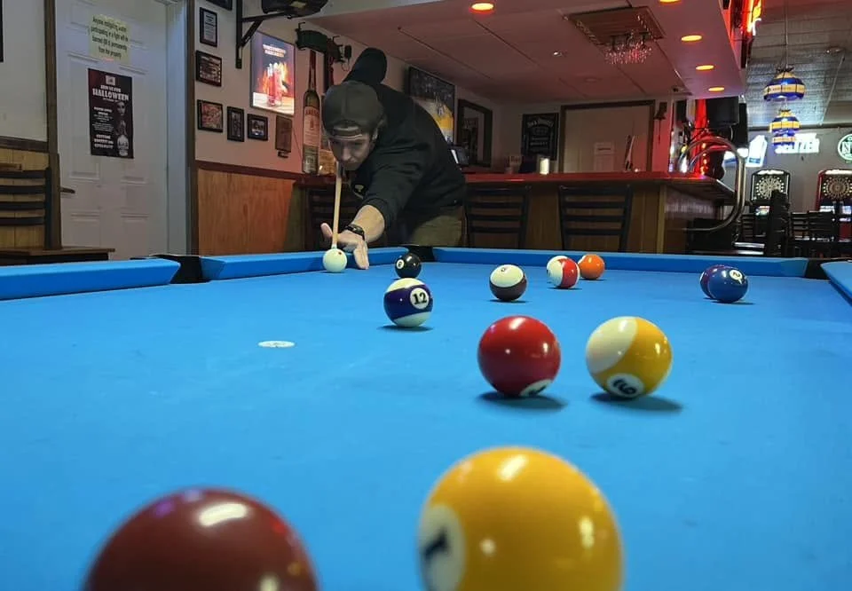 A person playing pool on a blue billiards table in a bar or pub with colorful lights and decorations.