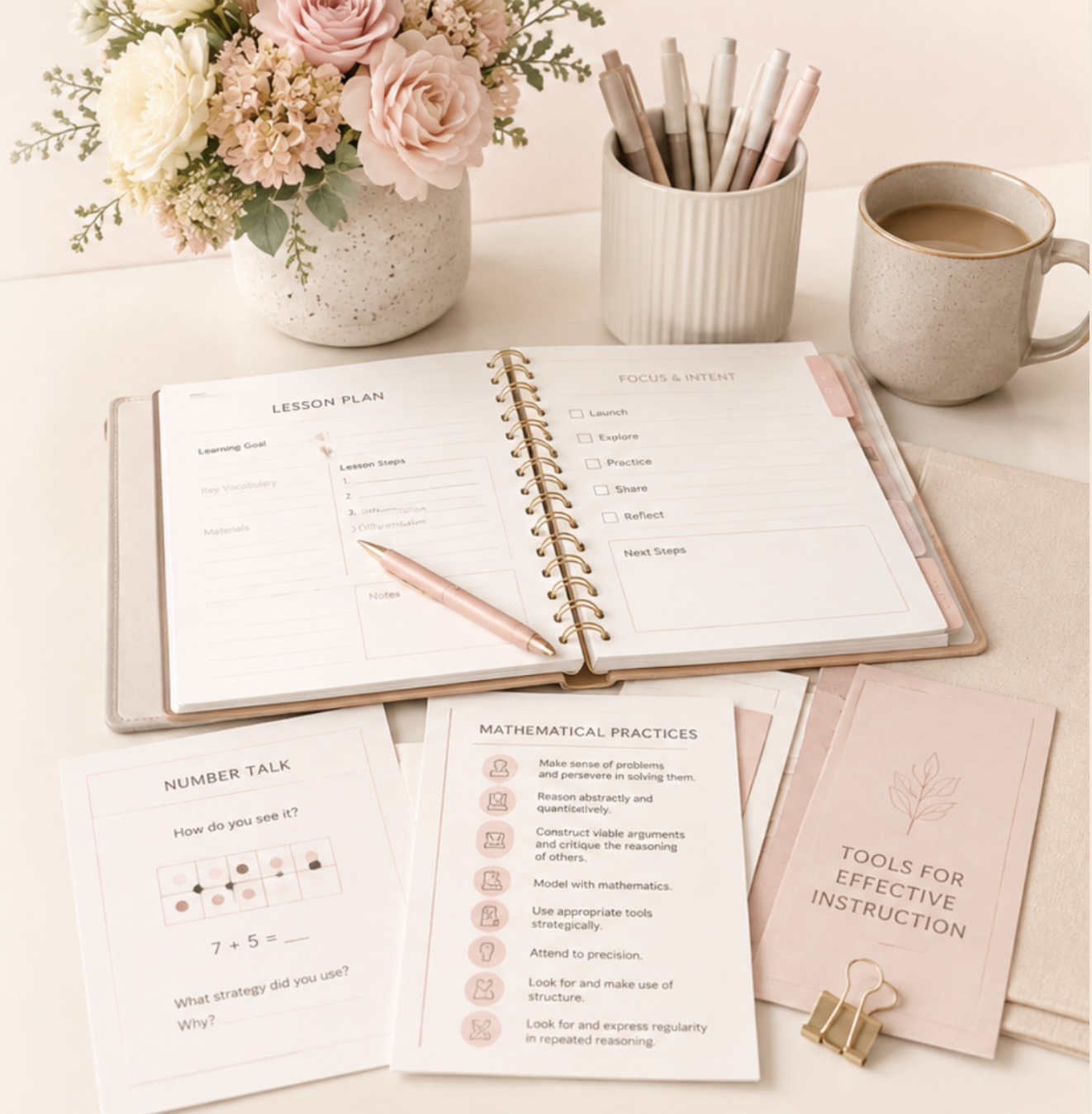 Open notebook with lesson plan and focus and intent sections, pink pen resting on pages, math practice sheets, a cup filled with pens and markers, a ceramic mug of coffee, a vase with pink and white flowers, pink folder, and a gold binder clip placed on a white surface.
