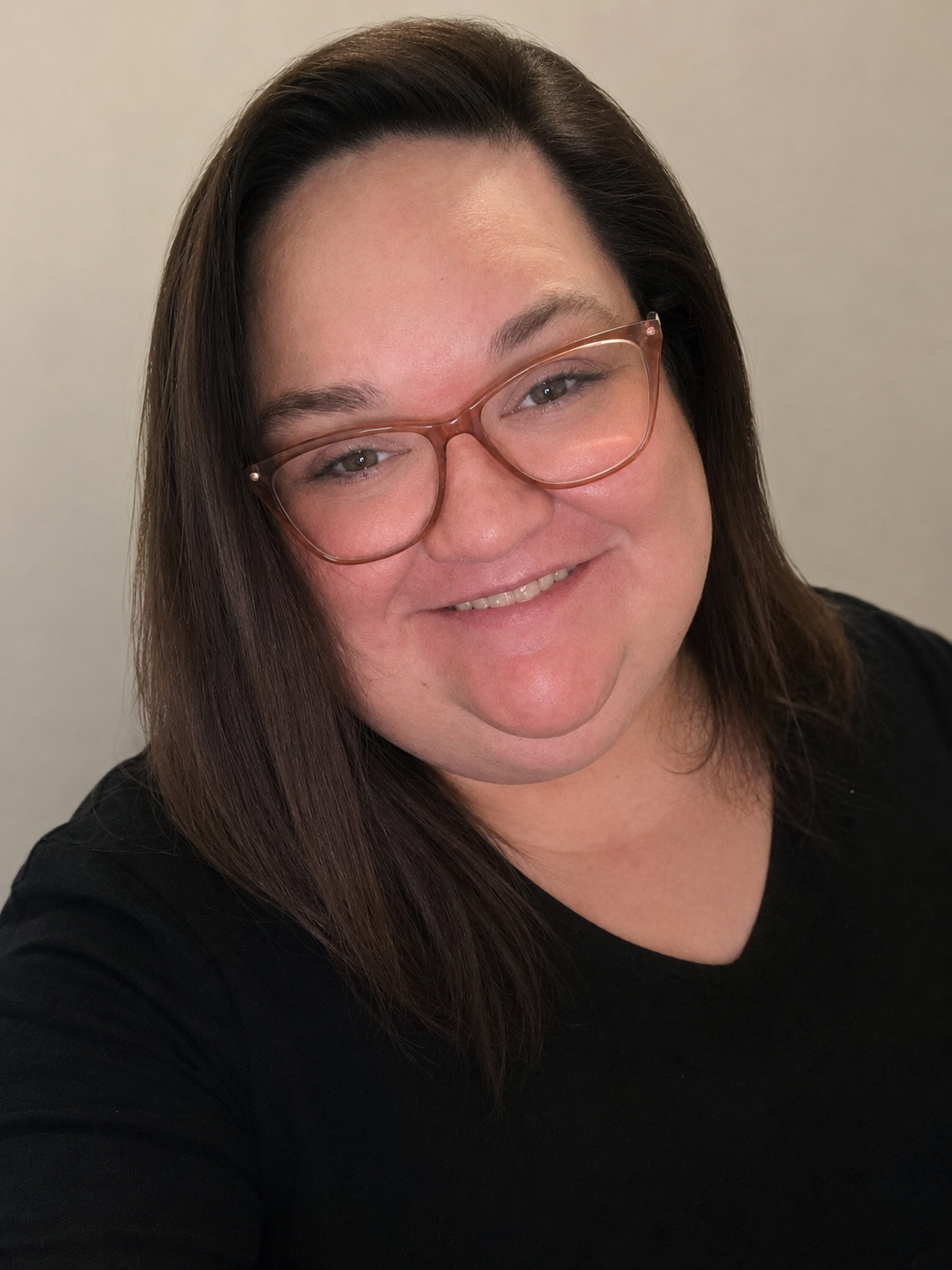 A woman with shoulder-length brown hair, wearing pink glasses and a black top, smiling at the camera.