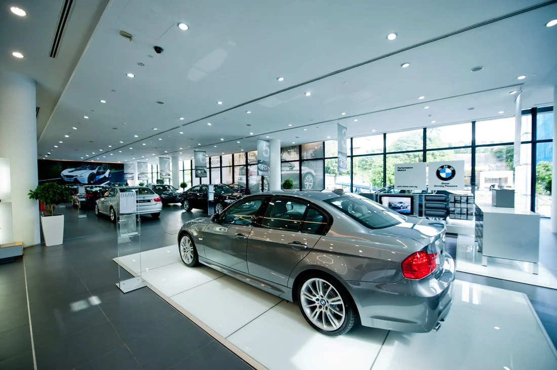 A showroom filled with various BMW cars, with large windows letting in natural light, displaying a sleek gray BMW sports car in the foreground.