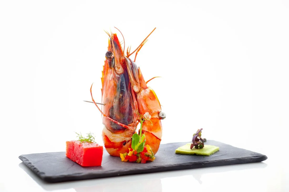 Gourmet seafood dish with lobster, watermelon, and garnishes on a black slate plate.
