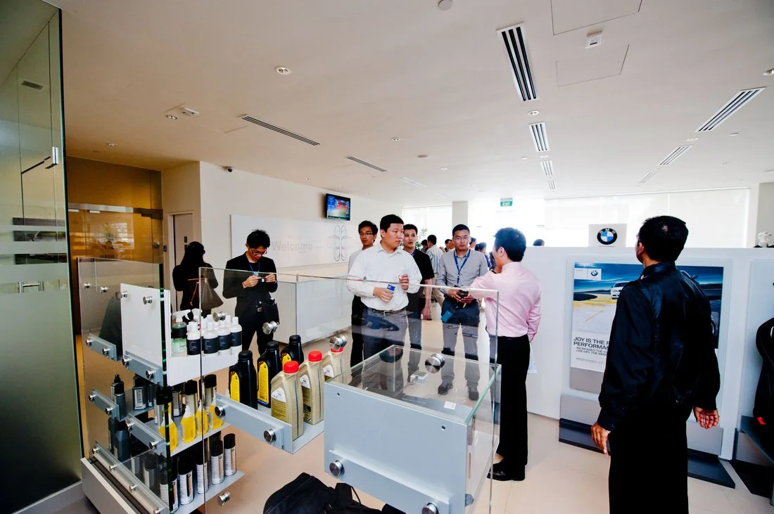 Car dealership showroom with BMW branding, display of car care products, and a sales representative speaking to a group of customers.