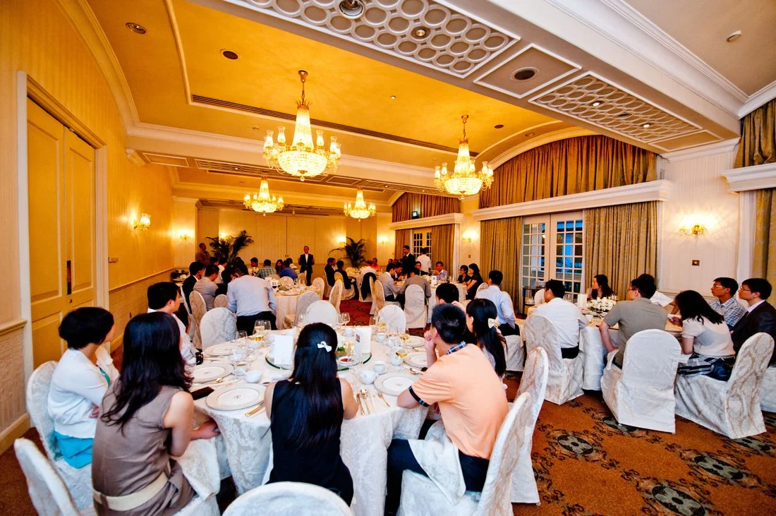 A banquet hall with chandeliers, decorated for a formal event, with guests seated at round tables.