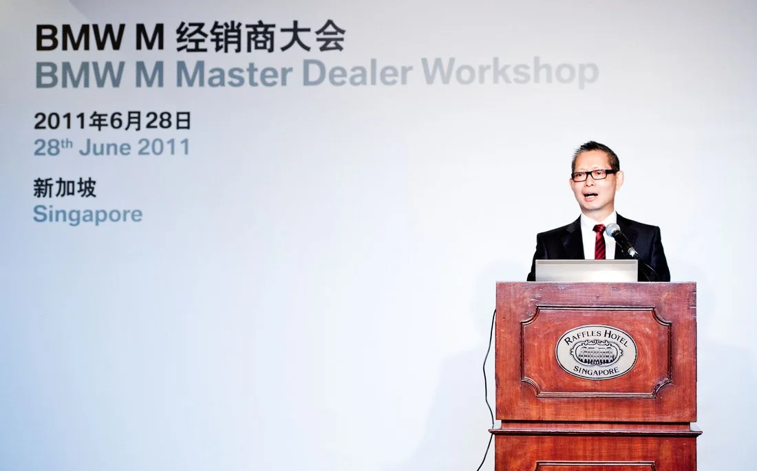 A man in a suit and glasses speaking at a podium during the BMW M Master Dealer Workshop at Raffles Hotel in Singapore on June 28, 2011.