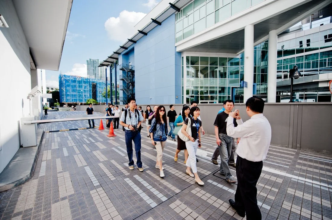 Group of people walking outside a modern office building, listening to a man speaking.