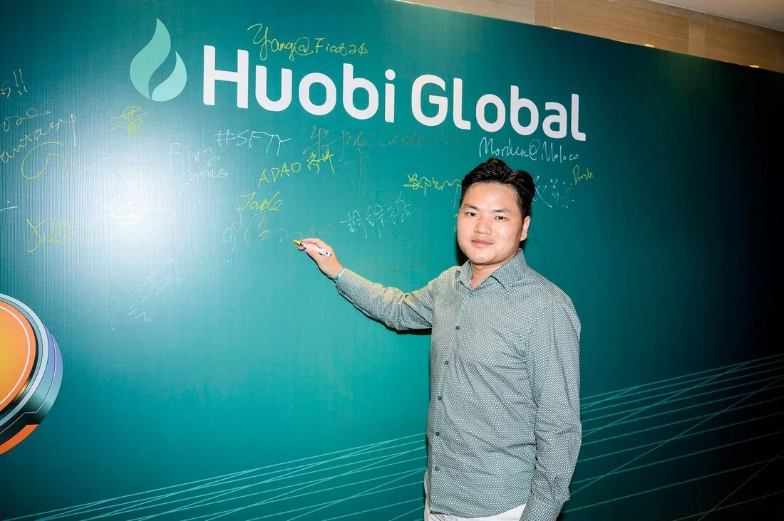 A man signing his name on a green Huobi Global promotional wall
