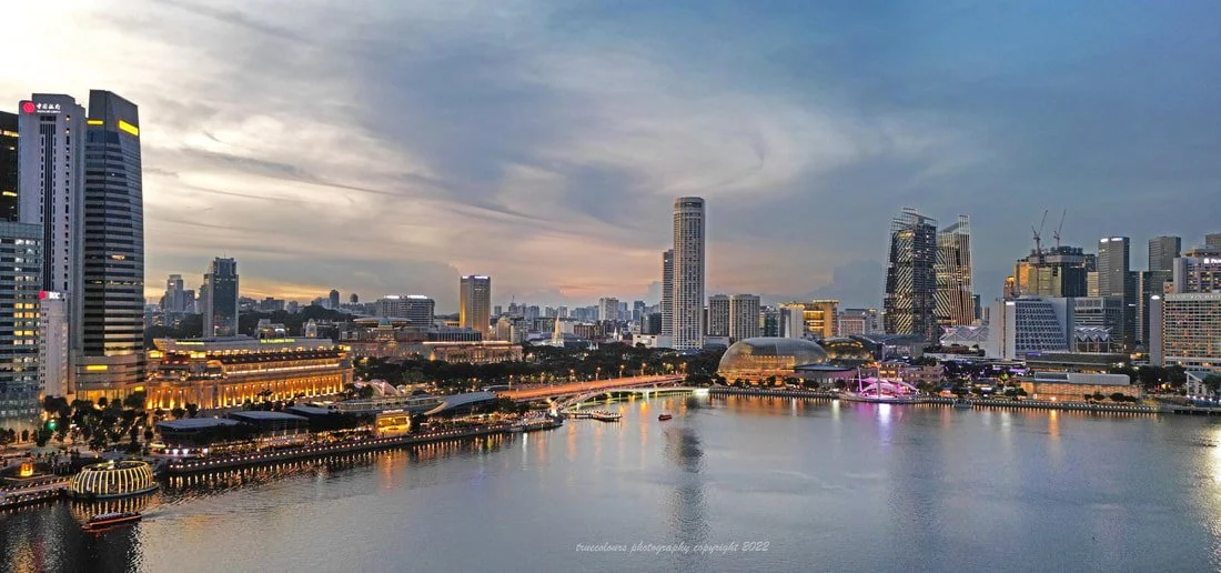 Singapore city skyline at sunset with modern skyscrapers, a river in the foreground, and a boat on the water.