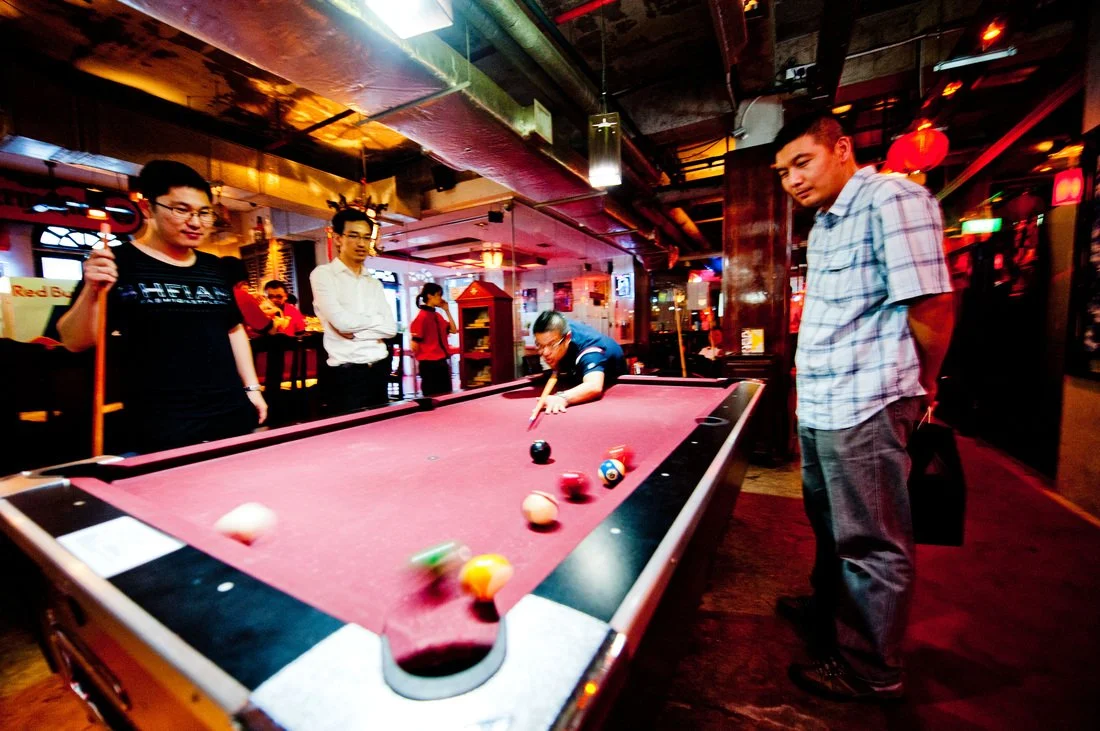 People playing pool in a bar or pub with colorful and dim lighting.