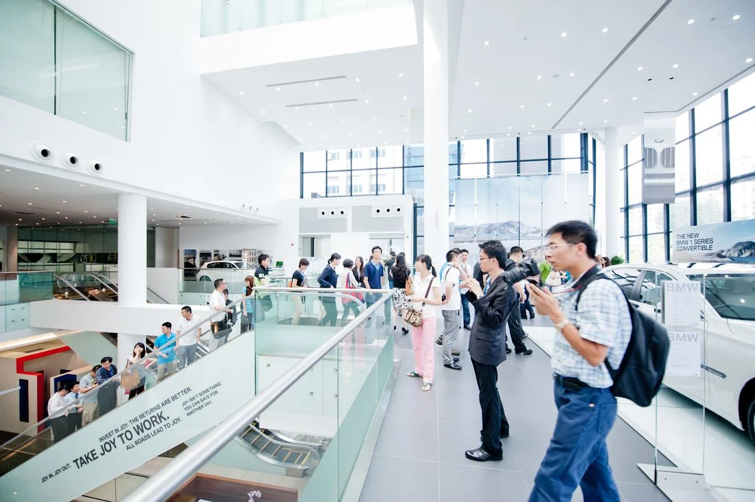 People inside a modern car showroom with large windows, displaying BMW vehicles and engaging in various activities.