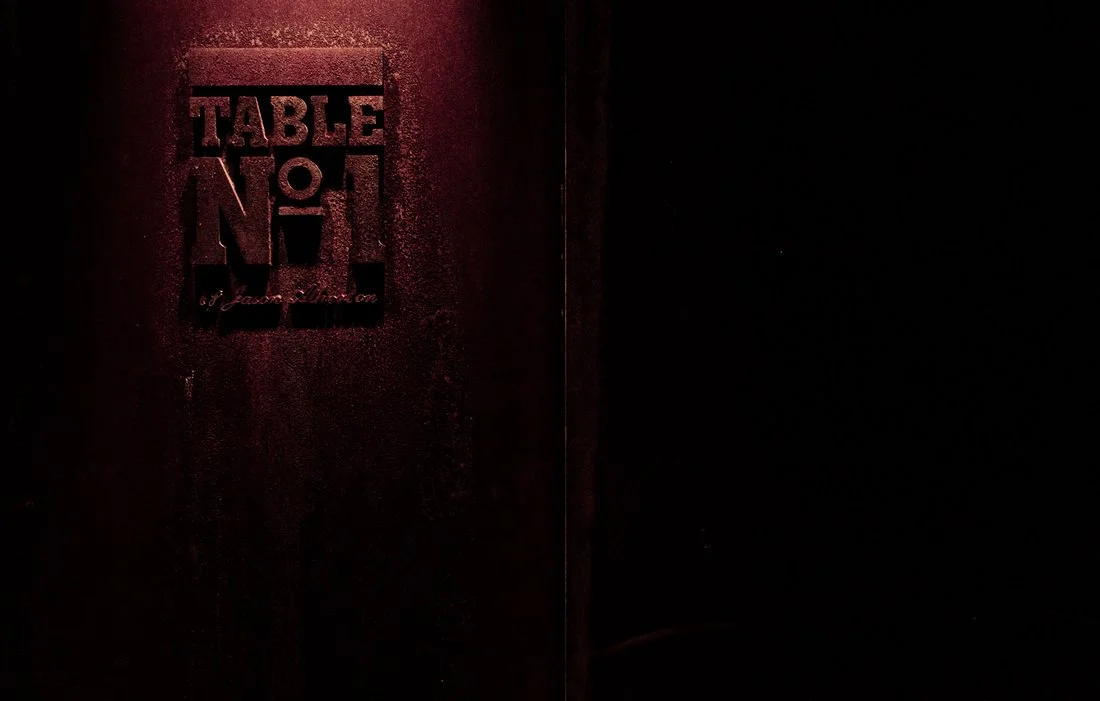 Dark wooden door with a sign that reads "TABLE NO 1" and a small lamp above it in a dimly lit setting.