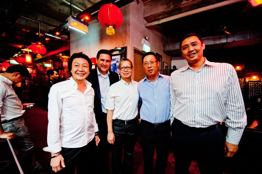 Group of five diverse people smiling at a social event with red lanterns and warm lighting.