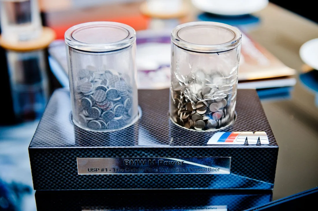 Two glass jars filled with small metal coins placed on a black container with a BMW M Power logo.