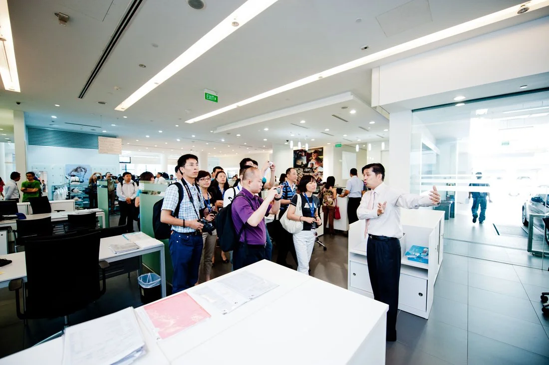 Tour guide explaining to a group of people inside a modern office or showroom.