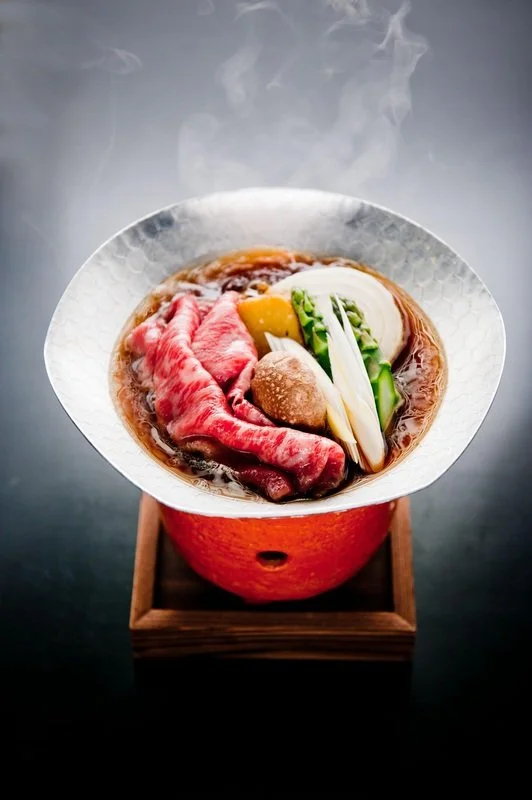 Steaming bowl of hot pot with slices of raw beef, vegetables, and mushrooms in broth