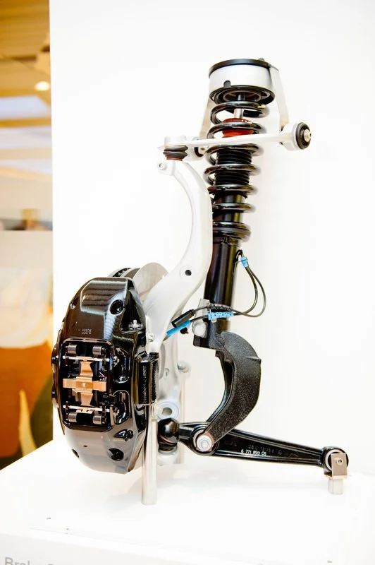 A car suspension system displayed on a white surface with a white background, showing the coil spring, shock absorber, and related components.