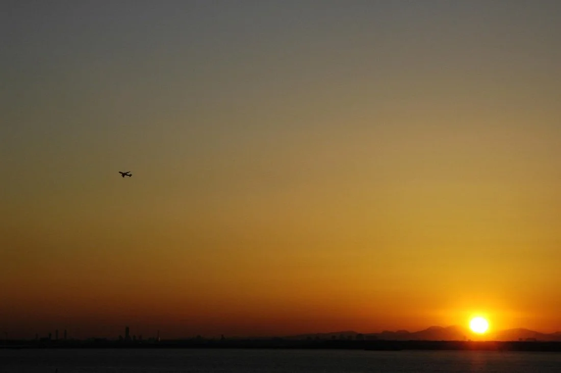 Sunset over water with a small airplane flying in the sky.