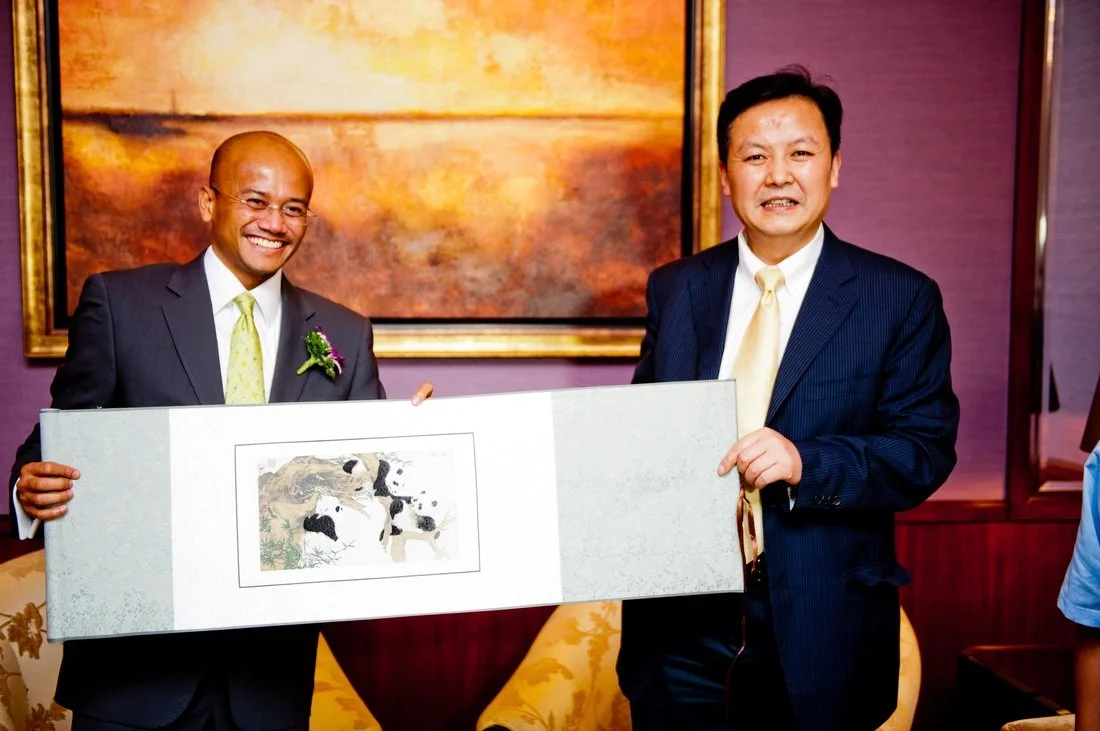 Two men in suits holding a framed artwork of pandas.