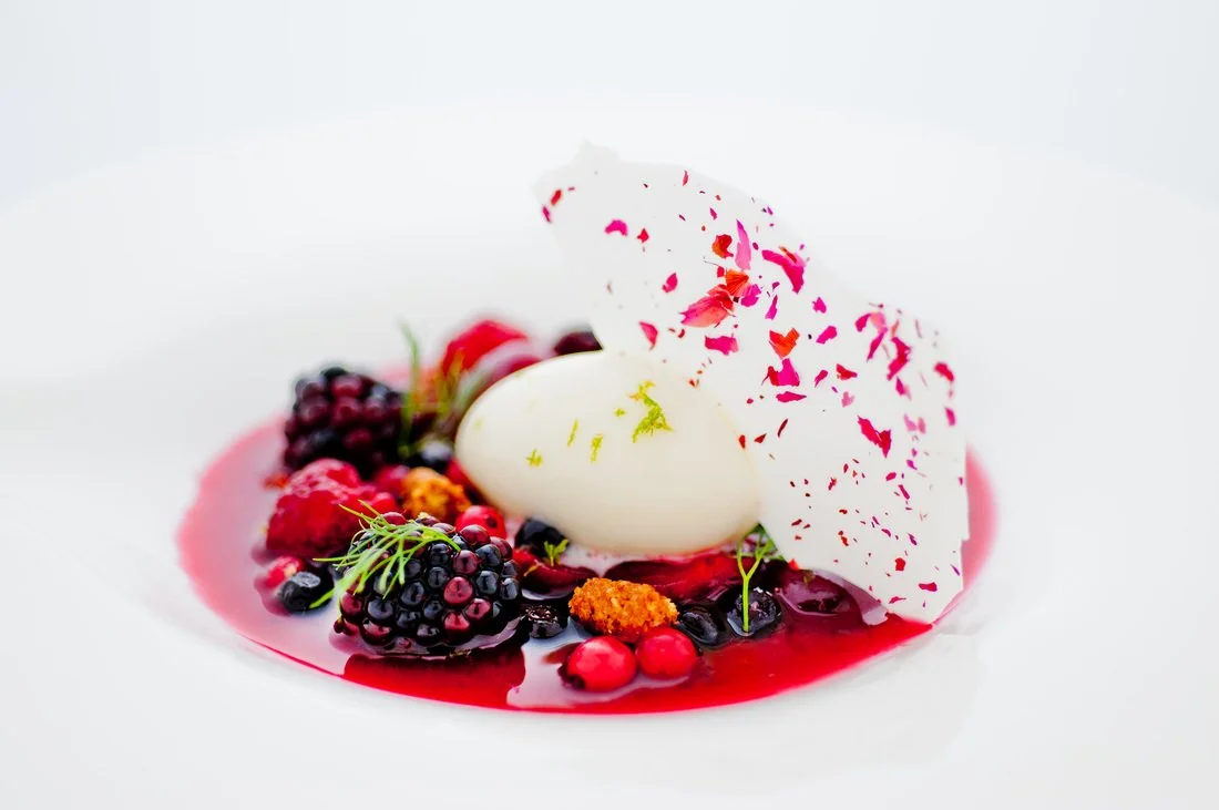 Dessert with mixed berries, cream, and a white decorative element on a white plate