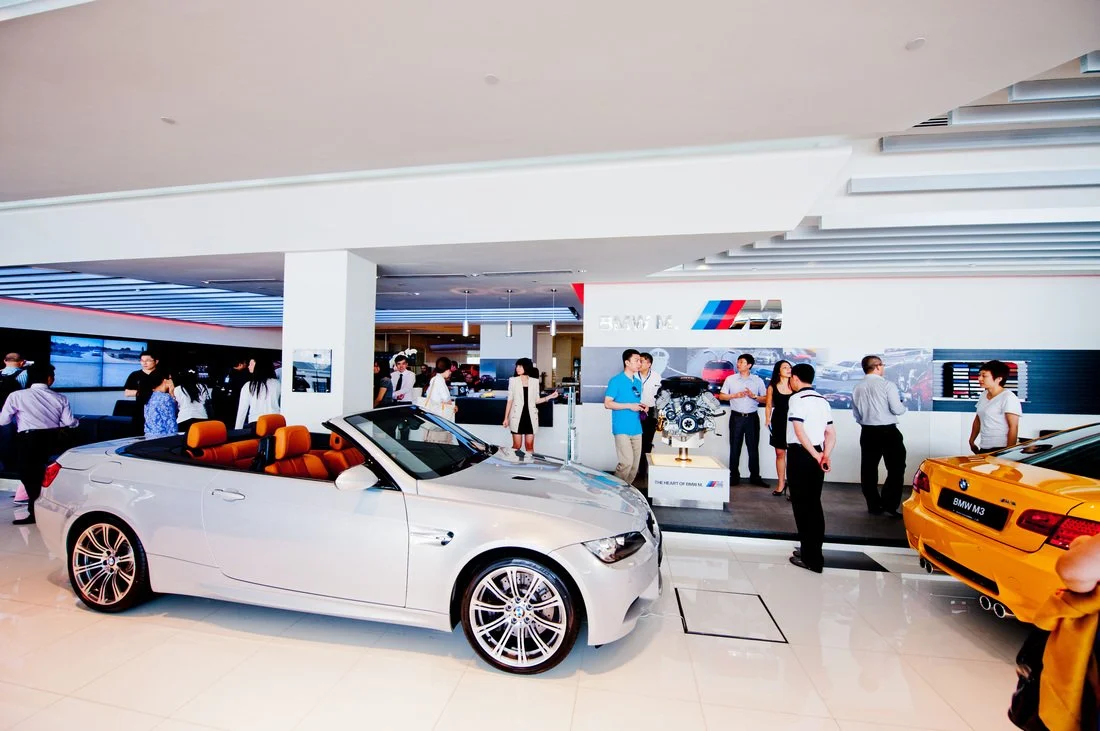 A car showroom with BMW vehicles on display, including a white convertible with orange interior and a yellow model.