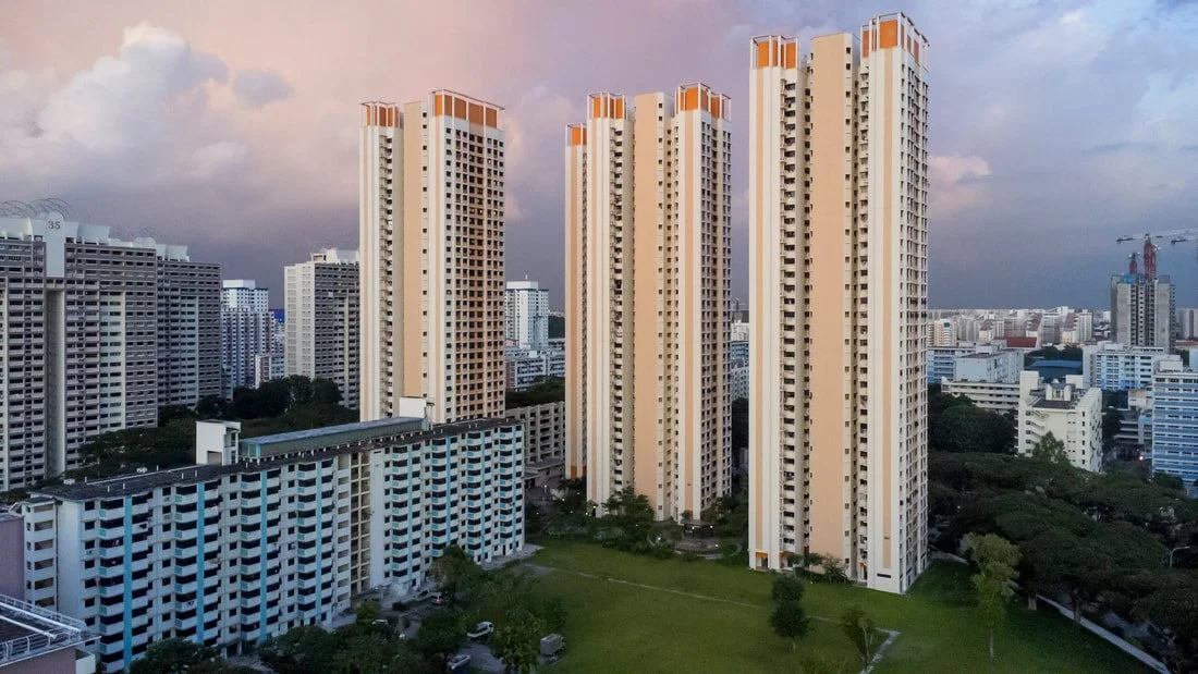Tall residential apartment buildings in an urban cityscape during sunset with a park in the foreground.
