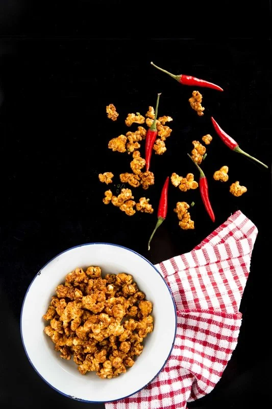A white bowl filled with crispy fried chicken pieces, red chili peppers, and a red and white checkered napkin on a black surface.