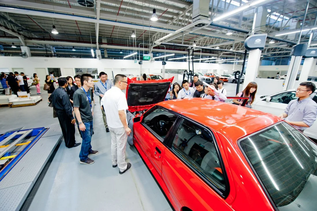Group of people inspecting a red car in an indoor showroom or workshop.