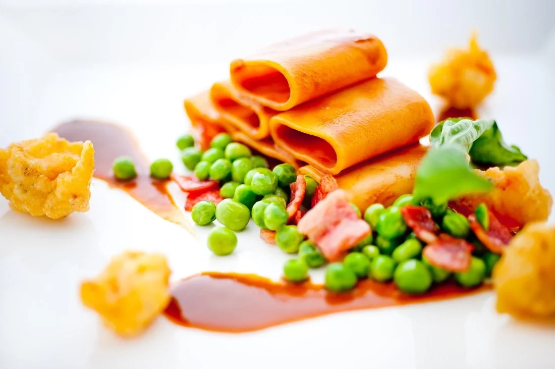 Gourmet plated meal with rolled cheese slices, green peas, bacon bits, assorted sauce, and crispy garnishes