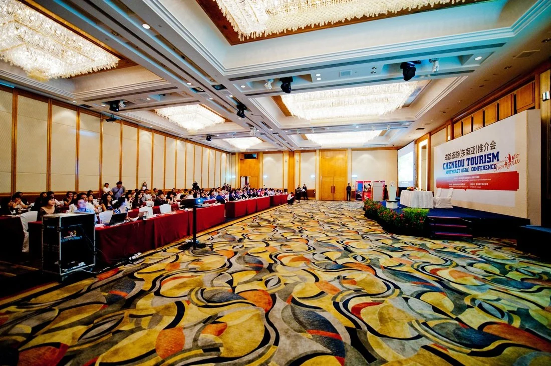 Conference room filled with attendees, a stage with a large screen, and a backdrop displaying 'Chengdu Tourism' at a travel conference.