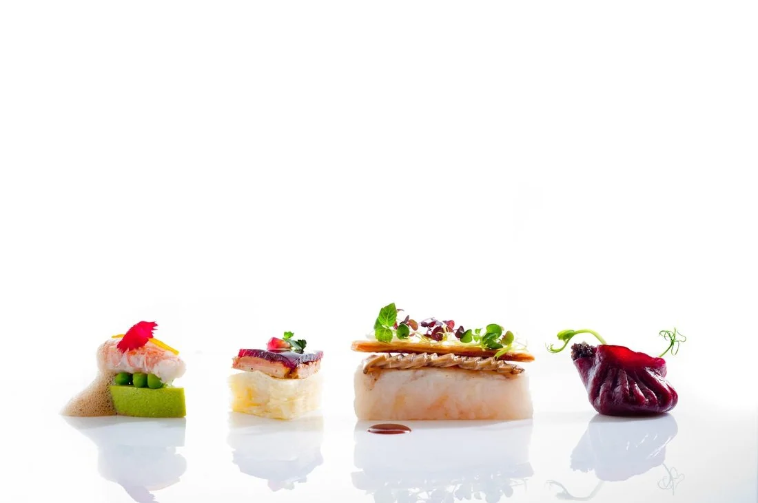 Four pieces of gourmet sushi with various toppings on a white background.