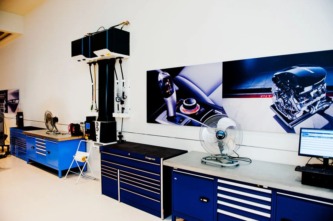 Workshop with car engine and automotive technology equipment, including a computer monitor, diagnostic tools, and automotive parts.