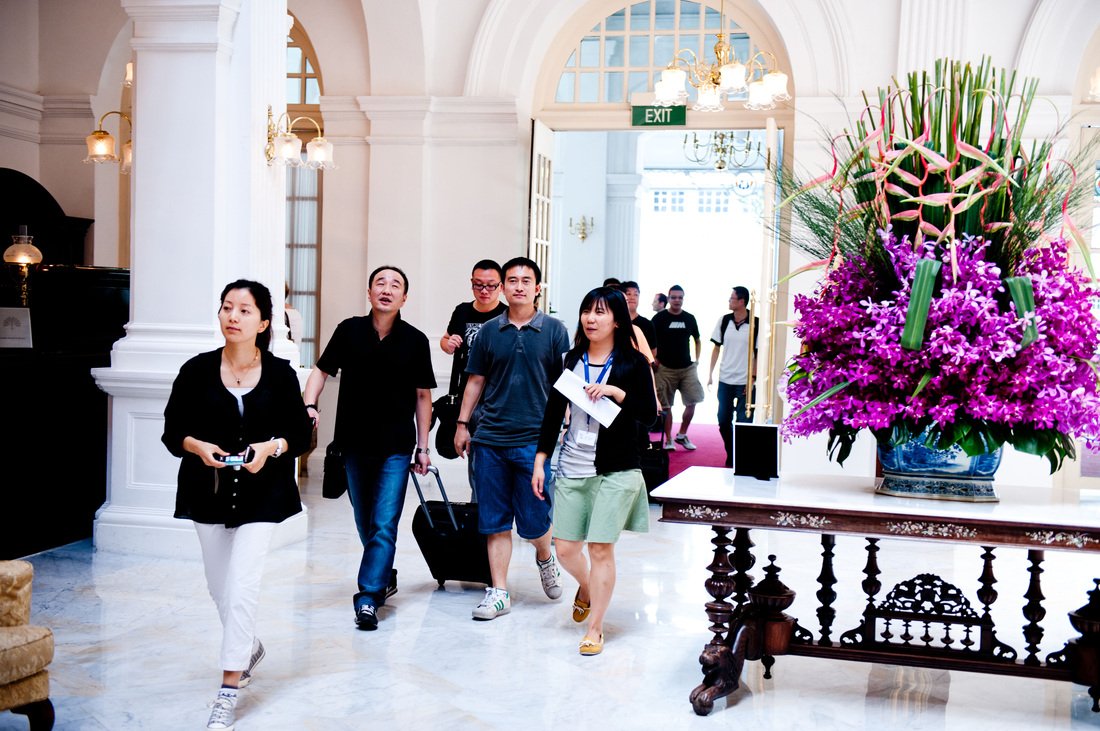 Group of people walking through a hotel lobby with large floral arrangement and elegant architecture.