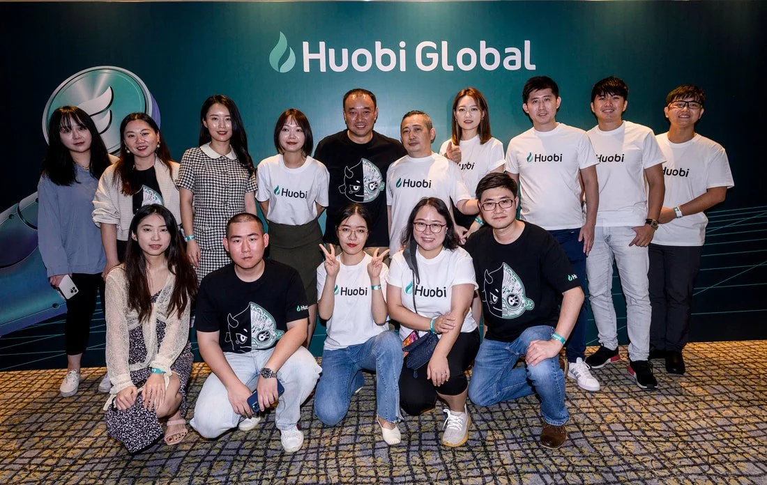 Group of people posing for a photo in front of a Huobi Global banner, some wearing Huobi t-shirts.