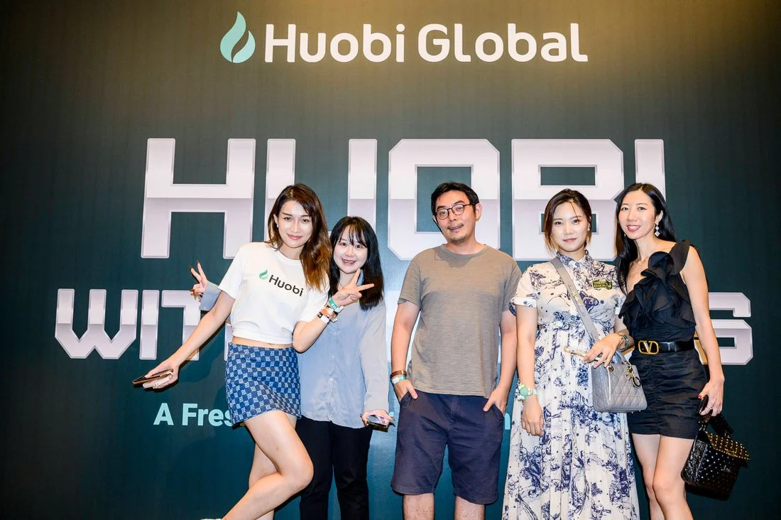 Group of five people posing in front of a Huobi Global banner at an event.